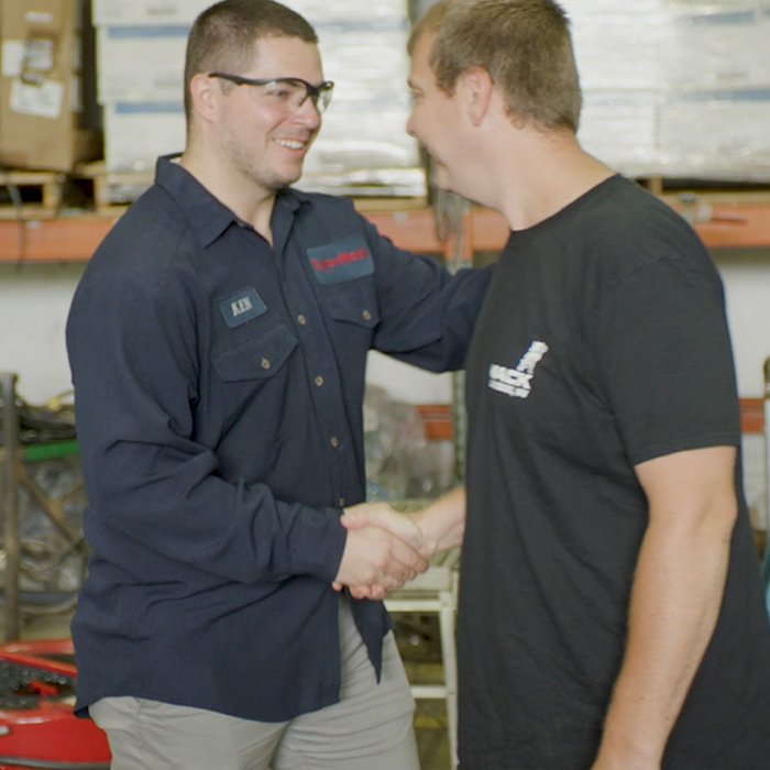 Two Mobil technicians in warehouse smiling and shaking hands
